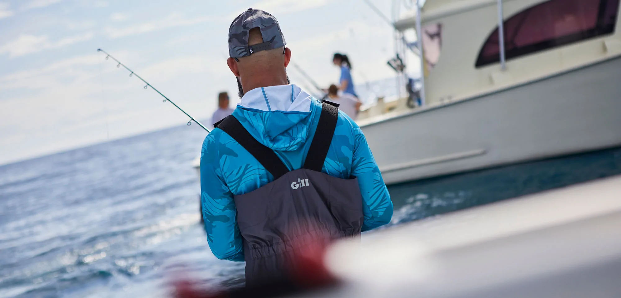 Angler on a boat in the sea wearing Gill with a fishing rod